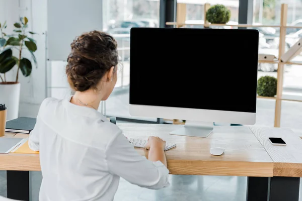 Back view of businesswoman working on computer with blank screen in office — Stock Photo
