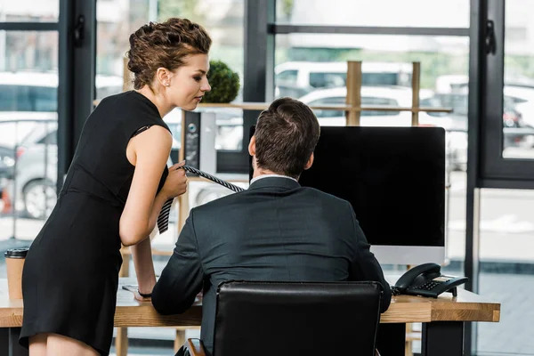 Молодая деловая женщина держит коллег галстук во время флирта на рабочем месте в офисе — стоковое фото