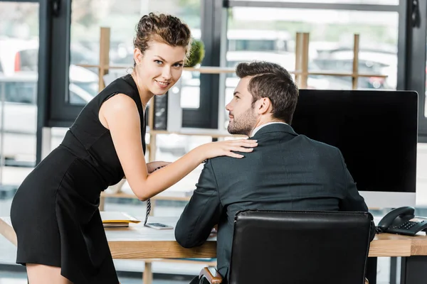 Junge Geschäftsfrau hält Kollegen Krawatte, während sie am Arbeitsplatz im Büro flirtet — Stock Photo