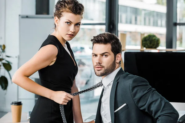 Side view of businesswoman holding colleagues tie while flirting at workplace in office — Stock Photo