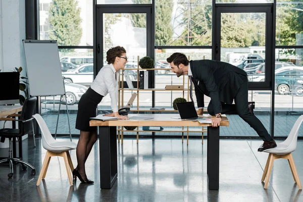 Seitenansicht eines Geschäftsmannes und einer Geschäftsfrau, die am Arbeitsplatz im Büro flirten — Stockfoto