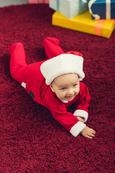 Adorable little baby in santa suit lying on red carpet — Stock Photo