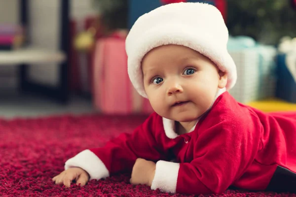 Close-up retrato de adorável pequeno bebê em santa chapéu deitado no chão e olhando para a câmera — Fotografia de Stock
