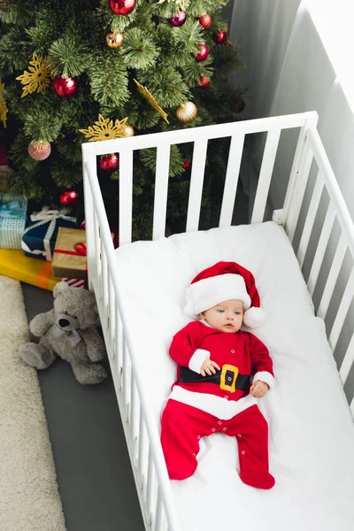 Visão de alto ângulo do bebê em terno de santa deitado na cama infantil — Fotografia de Stock