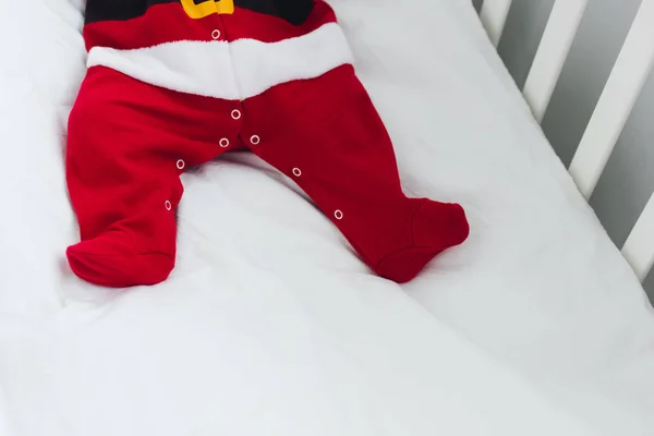 Tiro cortado de bebê pequeno em terno de santa deitado na cama infantil — Fotografia de Stock