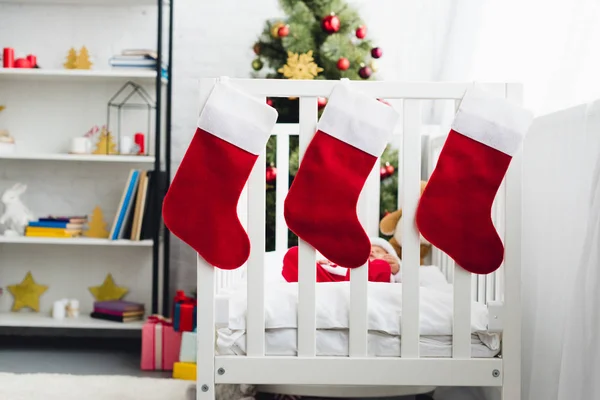 Gift socks hanging on infant bed with little baby in santa suit inside — Stock Photo