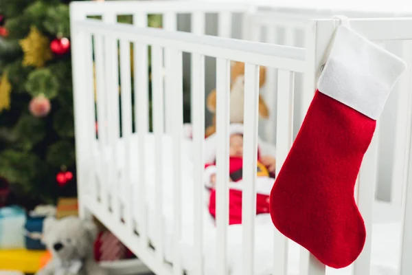 Little baby in santa suit lying in crib with christmas gift sock on foreground — Stock Photo