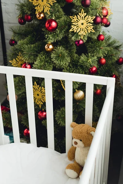 Vista de ángulo alto del oso de peluche en la cama infantil delante del árbol de Navidad - foto de stock