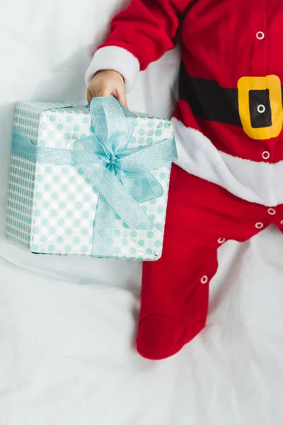 Schnappschuss eines kleinen Babys im Weihnachtsanzug, das mit Weihnachtsgeschenk in der Krippe liegt — Stockfoto