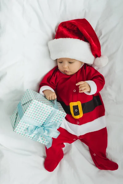 Top view of adorable little baby in santa suit lying in crib with christmas gift — Stock Photo