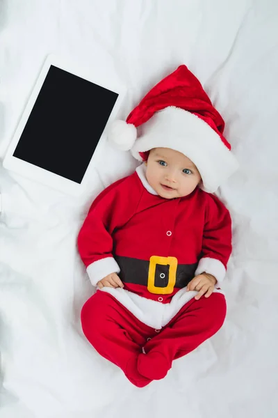 Vista superior do bebê pequeno feliz em terno de santa deitado no berço com tablet — Fotografia de Stock