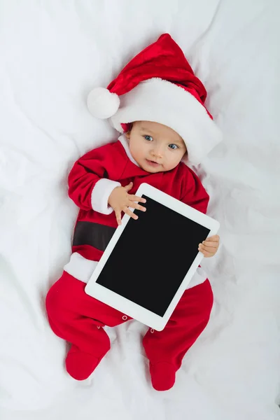 Vista superior de adorable bebé en traje de santa acostado en cuna con tableta - foto de stock