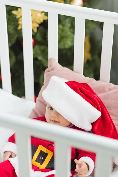High angle view of adorable little baby in santa suit lying in crib — Stock Photo
