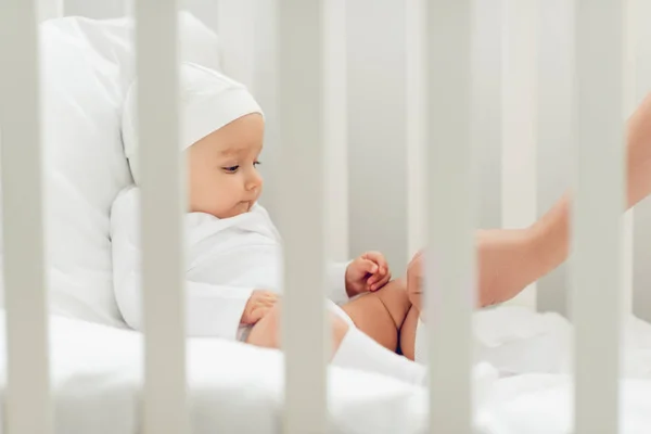 Adorable little baby in white hat sitting in crib — Stock Photo