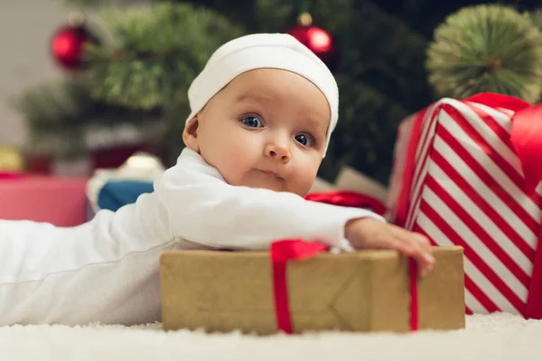 Close-up retrato de adorável bebê deitado no chão com presentes de Natal e olhando para a câmera — Fotografia de Stock