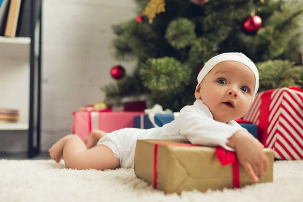 Schönes kleines Baby auf dem Boden liegend mit Weihnachtsgeschenken — Stockfoto