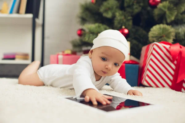 Красивый маленький ребенок с табличкой лежит на полу возле рождественских подарков и елки — стоковое фото