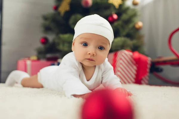Entzückendes kleines Baby auf dem Boden liegend mit Weihnachtsbaum im Hintergrund verschwommen — Stockfoto