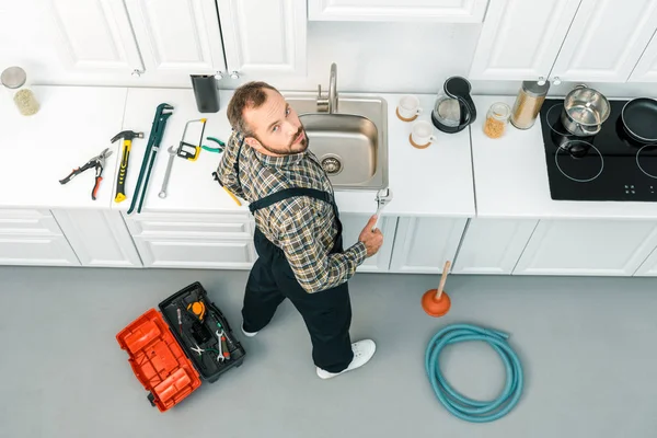 Hochwinkelaufnahme des hübschen Klempners mit verstellbarem Schraubenschlüssel und Blick auf die Kamera in der Küche — Stockfoto