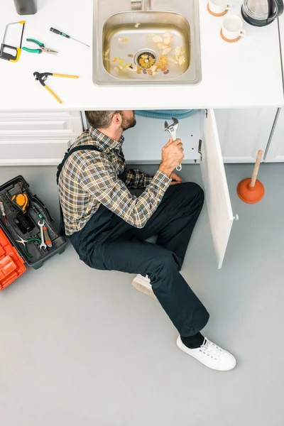 Visão de alto ângulo da pia de reparação de encanador com chave ajustável na cozinha — Fotografia de Stock