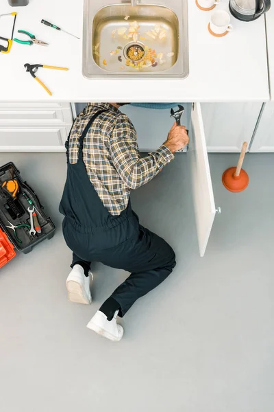 Hochwinkel-Ansicht des Klempners Reparatur defekter Spüle mit einstellbarem Schraubenschlüssel in der Küche — Stockfoto