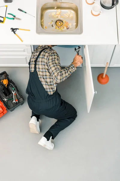 Visão de alto ângulo do encanador reparando pia quebrada com chave ajustável na cozinha — Fotografia de Stock