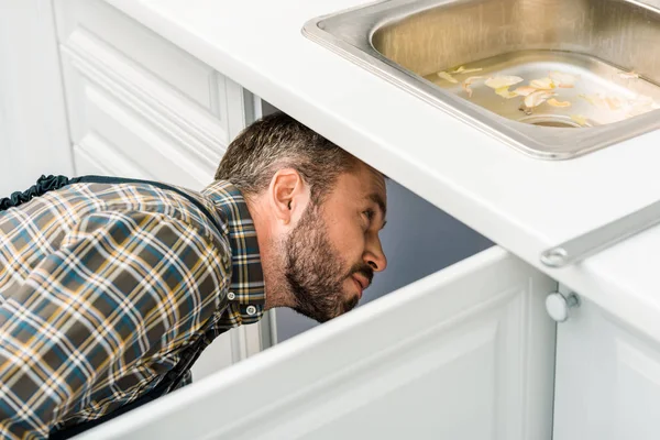 Klempner sucht unter defekter Spüle in Küche — Stock Photo