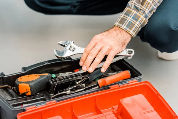 Abgeschnittenes Bild eines Klempners, der einen verstellbaren Schraubenschlüssel aus dem Werkzeugkasten in der Küche nimmt — Stockfoto