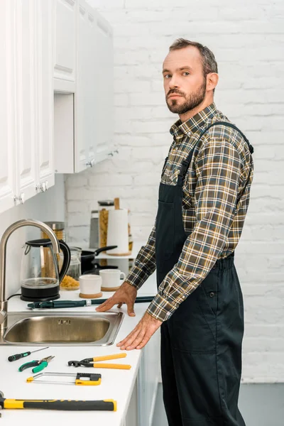 Handsome plumber standing near broken sink in kitchen and looking at camera — Stock Photo
