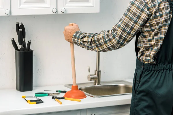 Обрезанный образ сантехника, принимающего вантуз на кухне — стоковое фото