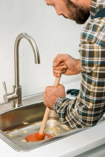 Bearded plumber using plunger and cleaning sink in kitchen — Stock Photo