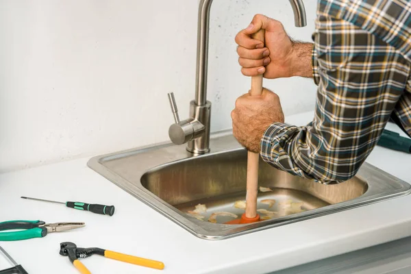 Image recadrée de plombier en utilisant le piston et l'évier de nettoyage dans la cuisine — Photo de stock