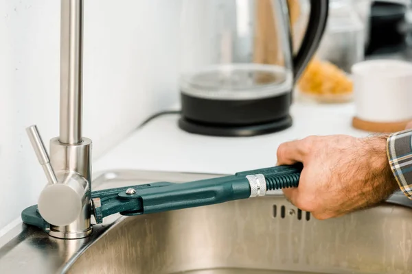 Cropped image of plumber repairing tap with monkey wrench in kitchen — Stock Photo