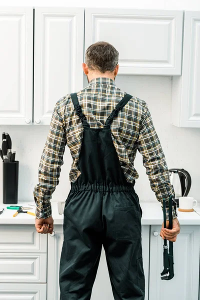 Back view of plumber holding monkey wrench and looking at sink in kitchen — Stock Photo