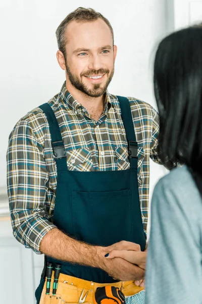 Sonriente fontanero guapo y cliente estrechando las manos en la cocina - foto de stock