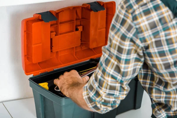 Imagen recortada de fontanero tomando llave ajustable de la caja de herramientas en la cocina - foto de stock