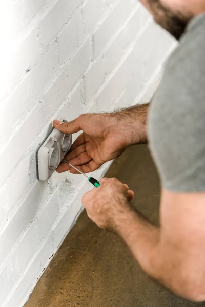Cropped image of electrician repairing and unscrewing power socket with screwdriver at home — Stock Photo