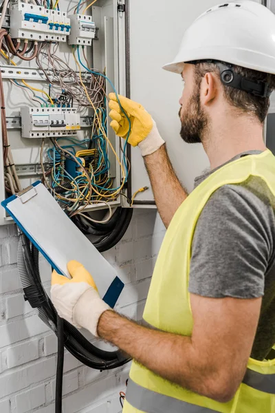 Elettricista che tiene appunti e controlla i fili nella scatola elettrica nel corridoio — Foto stock