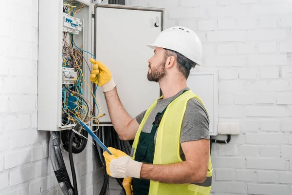 Vista laterale dell'elettricista che tiene appunti e controlla i fili nella scatola elettrica nel corridoio — Foto stock