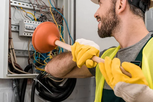 Lächelnder Elektriker repariert Stromkasten mit Kolben im Flur — Stockfoto