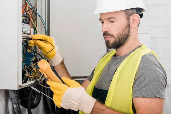 Schöner Elektriker überprüft Schalttafel mit Multimeter im Flur — Stockfoto