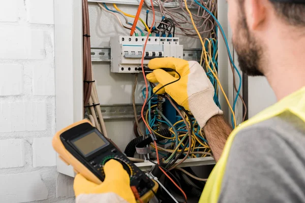 Cropped image of electrician checking electrical box with multimetr in corridor — Stock Photo