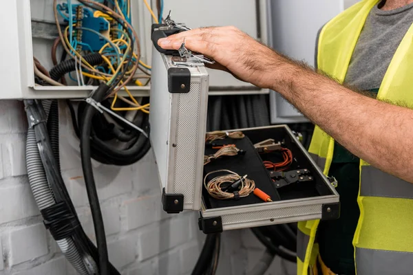 Abgeschnittenes Bild eines Elektrikers, der einen Werkzeugkasten in der Nähe eines Stromkastens im Flur hält — Stockfoto