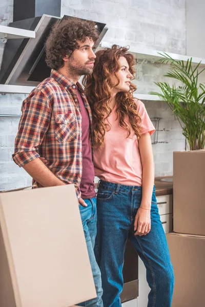 Pareja de pie cerca de cajas de cartón y mirando hacia otra cocina - foto de stock