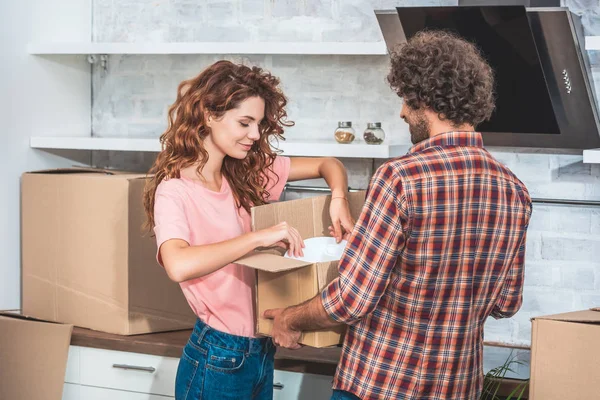 Пара берет посуду из картонной коробки на новой кухне — стоковое фото