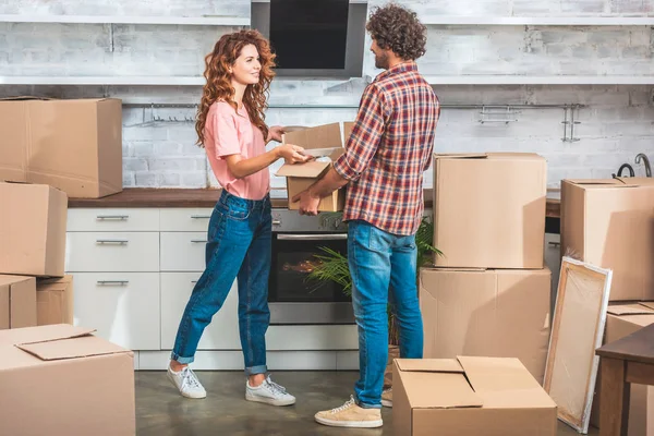 Side view of couple unpacking utensil from cardboard box at new kitchen and looking at each other — Stock Photo