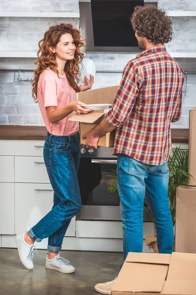 Casal desembalagem utensílio de caixa de papelão na nova cozinha e olhando um para o outro — Fotografia de Stock