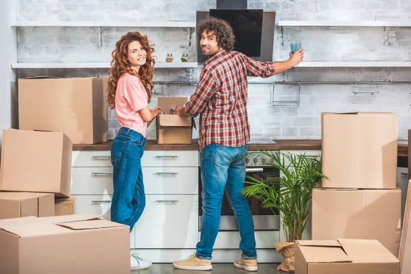 Smiling couple unpacking cardboard boxes at new kitchen and looking at camera — Stock Photo