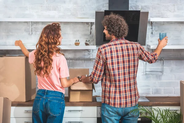 Vista trasera de las cajas de cartón de desembalaje de pareja en el nuevo hogar - foto de stock