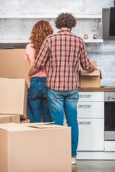 Rückansicht des Paares beim Umarmen und Auspacken von Pappkartons in neuer Küche — Stockfoto